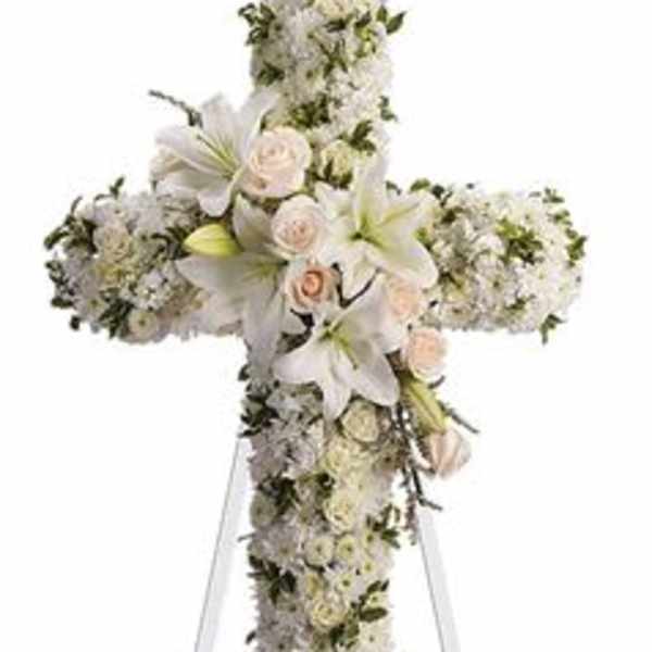White floral cross arrangement on a stand with pale pink roses and lilies