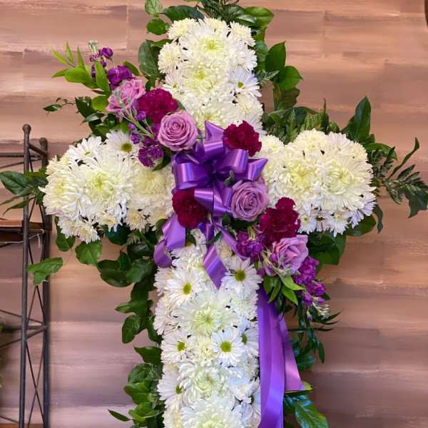 Cross-shaped floral spray with white chrysanthemums, purple roses, and a purple ribbon