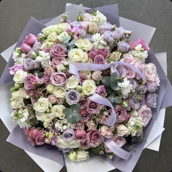 Large pastel bouquet of roses and white blooms wrapped in lavender paper