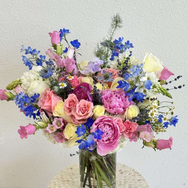 Colorful mixed bouquet of pink, blue, and white flowers in a glass vase
