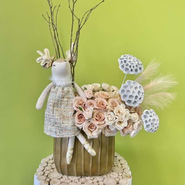 Floral arrangement with blush roses and a decorative bunny figure in a gold vase