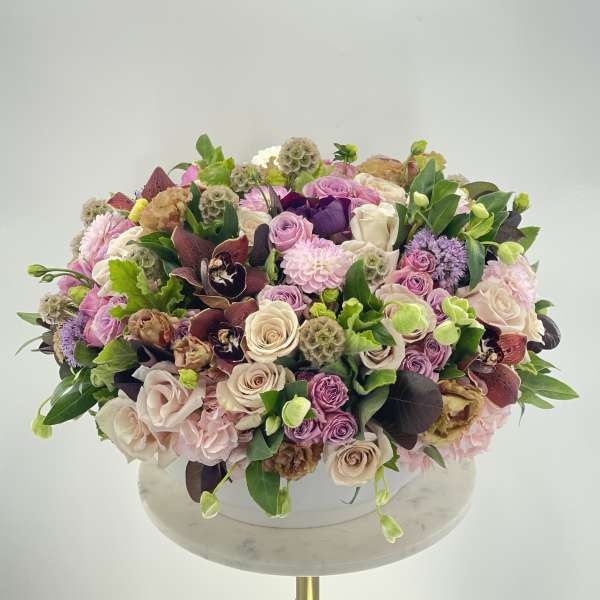 Large pastel bouquet with roses, orchids, and pink blooms in a white container