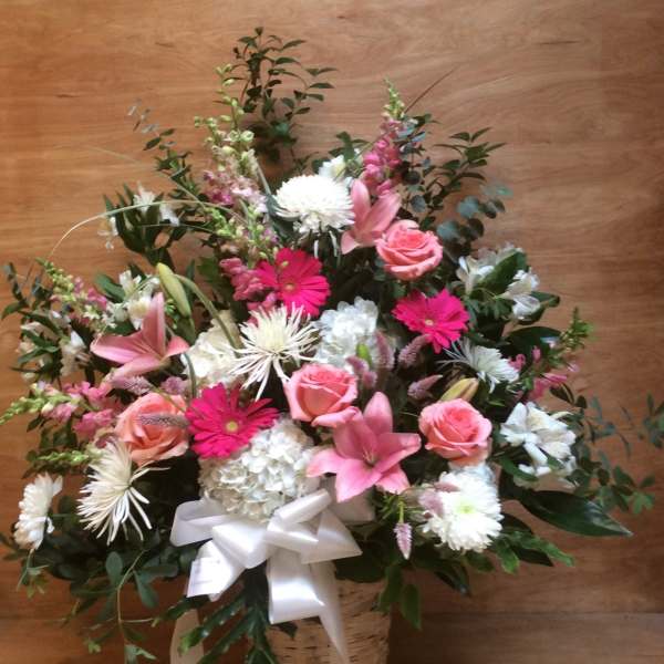 Pink and white mixed flower arrangement in a basket with a white ribbon