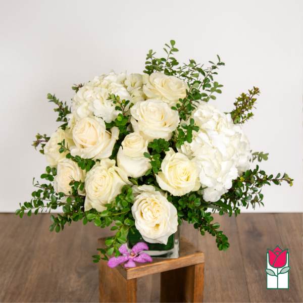 White roses and hydrangeas in a square glass vase with greenery