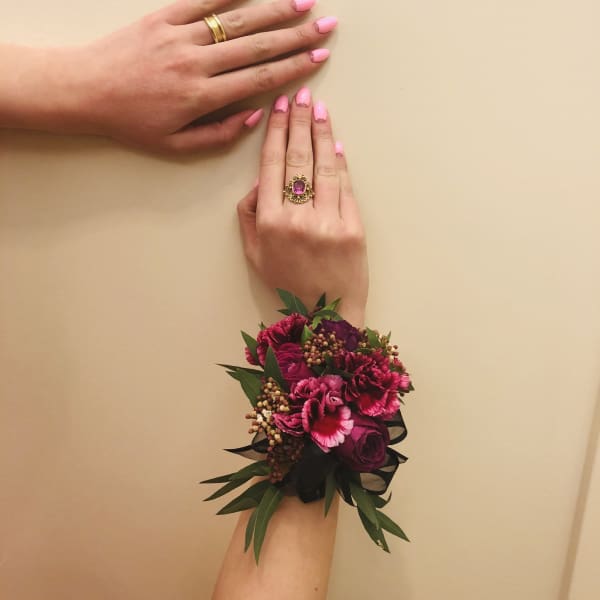 Pink floral wrist corsage with dark ribbon on a hand