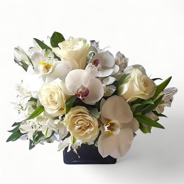 Low arrangement of ivory roses and white orchids in a black cube vase