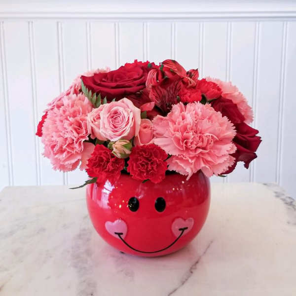 Pink and red flower arrangement in a smiley-face vase