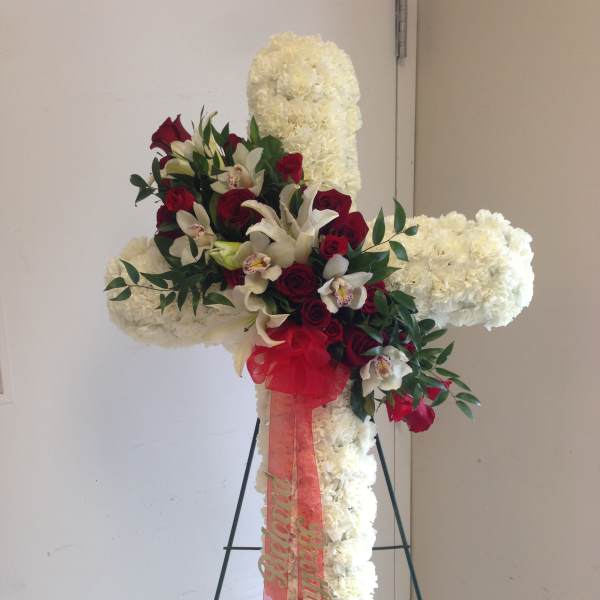 White floral cross on an easel with red roses and orchids