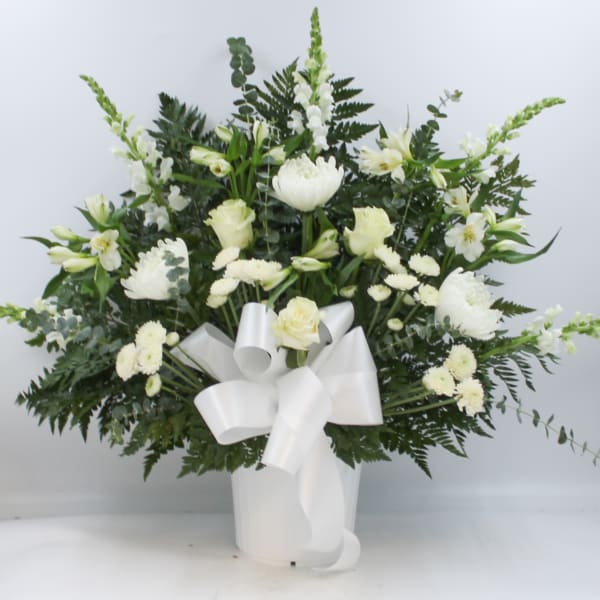 White floral arrangement in a white vase with a large ribbon bow