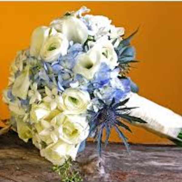 Hand-tied white and blue bridal bouquet with roses, calla lilies, hydrangea and thistle on a rustic surface