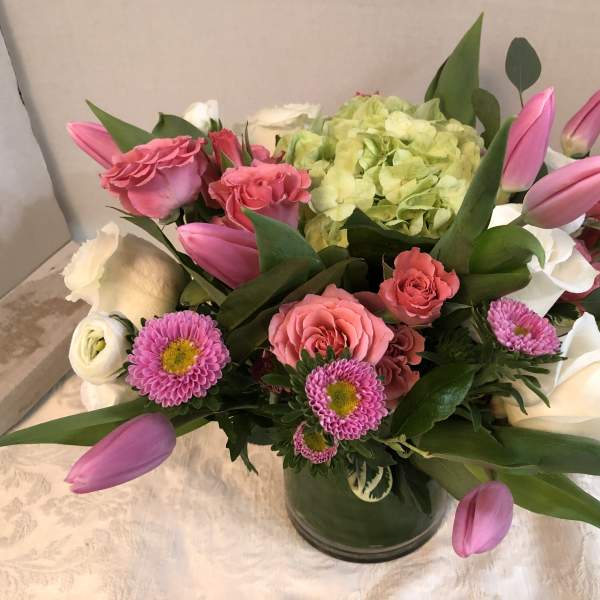 Pink tulips, roses, and white blooms arranged in a glass vase