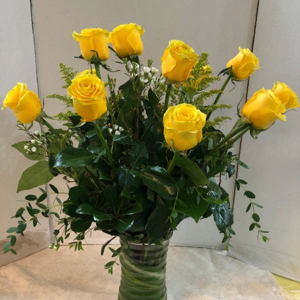 Yellow roses arranged in a clear glass vase with greenery
