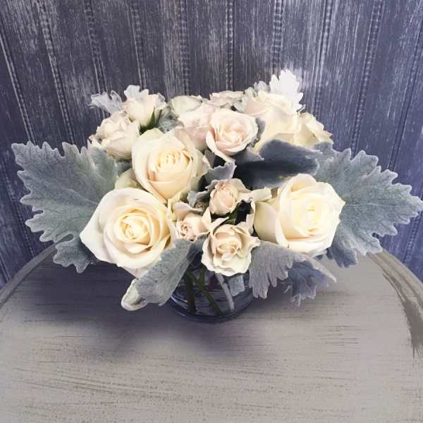 White roses arranged in a glass vase with silvery foliage