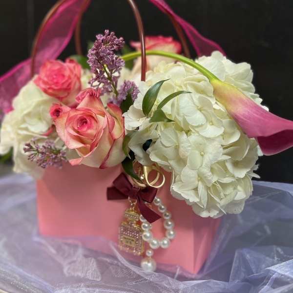 Pink roses and white hydrangeas in a pink gift basket with a ribbon handle