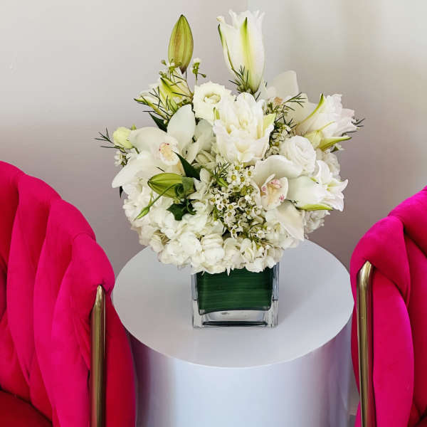White floral arrangement in a square glass vase on a round table