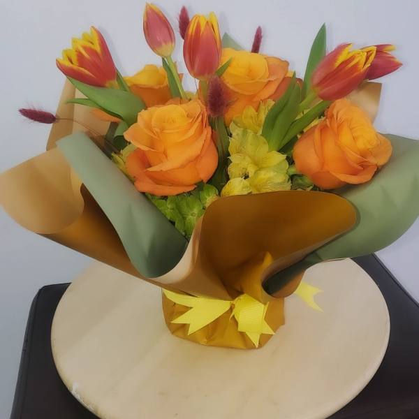 Bouquet of orange roses and red-yellow tulips wrapped in gold and green paper