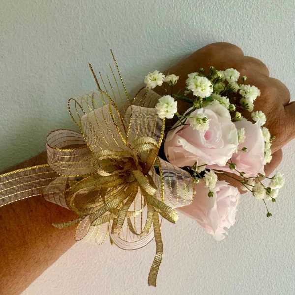 Small wrist corsage with pale pink roses and white baby's breath on gold ribbon