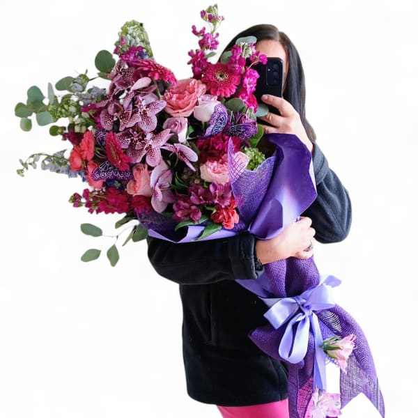 Person holding a large bouquet of pink and purple flowers wrapped in purple paper
