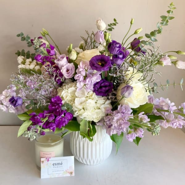 Purple and white bouquet in a white vase beside a candle