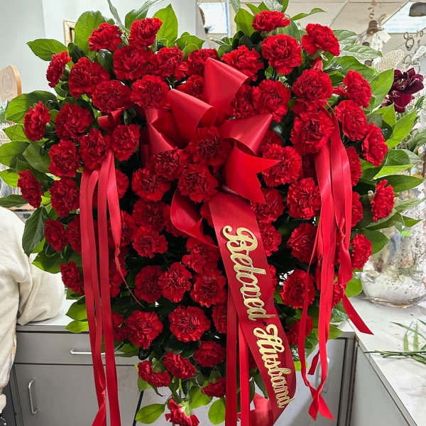 Heart-shaped standing spray of red carnations with ribbon