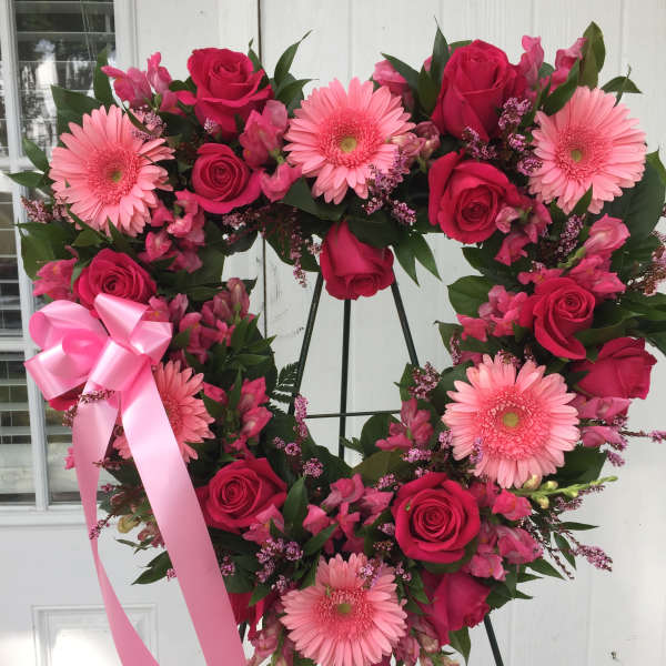 Heart-shaped wreath of pink roses and gerbera daisies with a pink ribbon