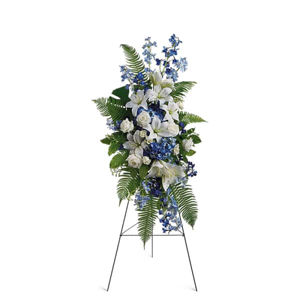 Standing floral spray with white lilies, blue flowers, and ferns on an easel