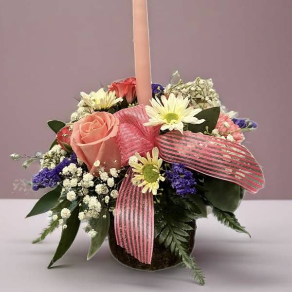 Pink candle in a mixed flower arrangement with a striped ribbon
