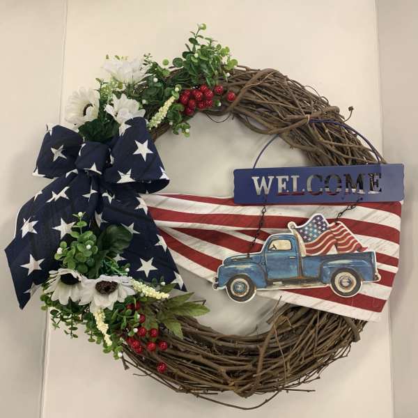 Patriotic wreath with white flowers, a star-spangled bow, and a blue truck sign