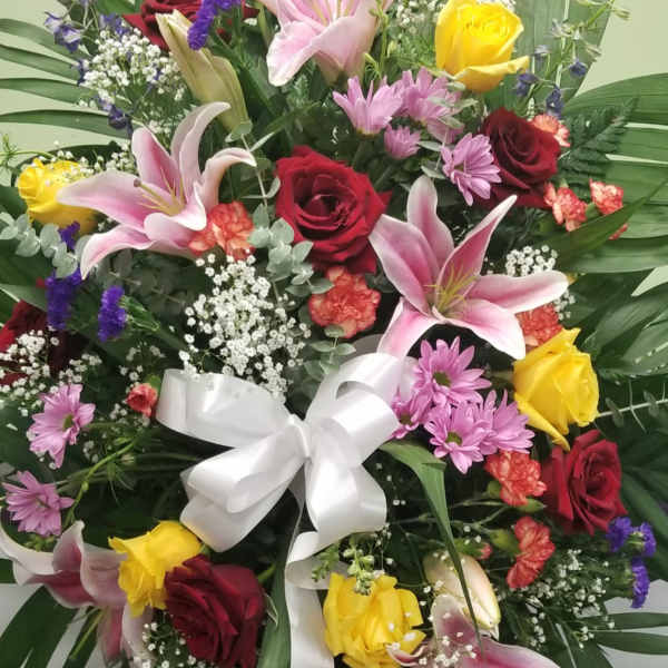 Standing floral spray with roses, lilies, and a white ribbon bow