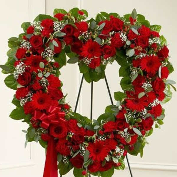 Heart-shaped red floral wreath on a stand with a red ribbon