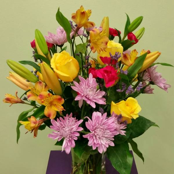 Mixed bouquet of yellow roses, lilies, and pink chrysanthemums in a glass vase