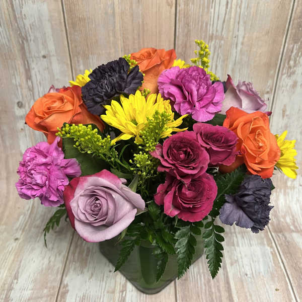 Colorful bouquet of roses, carnations, and yellow daisies in a glass vase