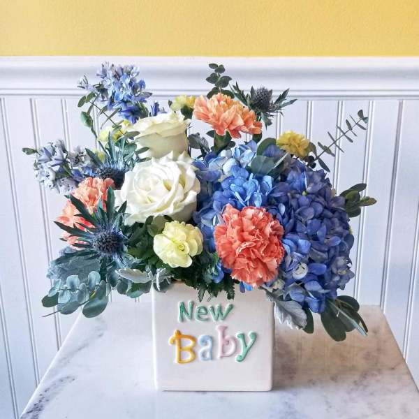 Colorful flower arrangement in a white vase labeled New Baby