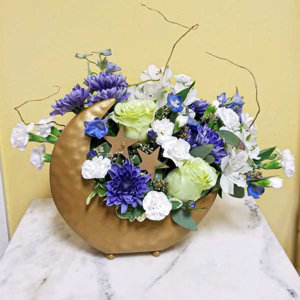 Purple and white floral arrangement in a gold crescent vase with star accents