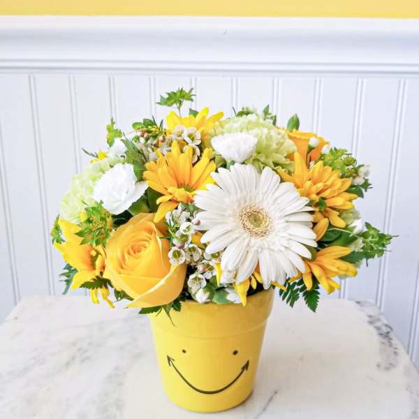 Yellow and white flower arrangement in a smiley-face pot