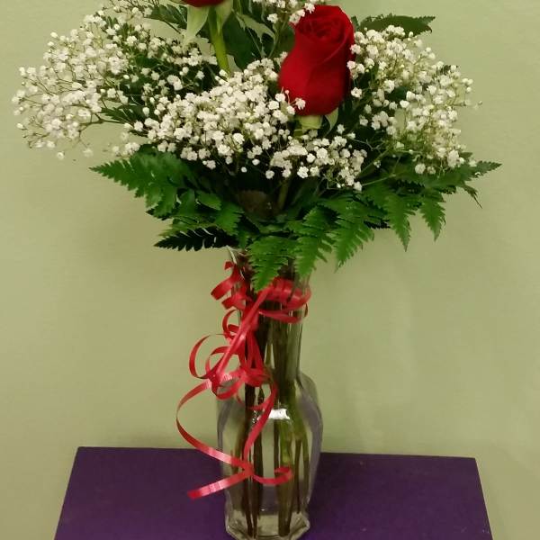 Three red roses in a clear glass vase with white baby's breath