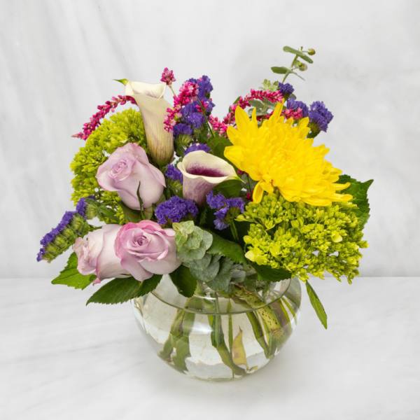 Mixed bouquet of roses, calla lilies, and chrysanthemums in a glass bowl vase