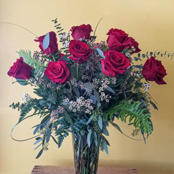 Red roses arranged in a clear glass vase with mixed greenery