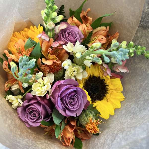 Bouquet of purple roses, sunflowers, and orange mixed blooms wrapped in paper