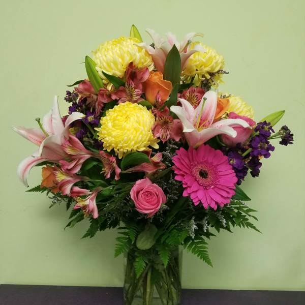 Mixed bouquet of lilies, roses, gerbera daisies, and chrysanthemums in a glass vase
