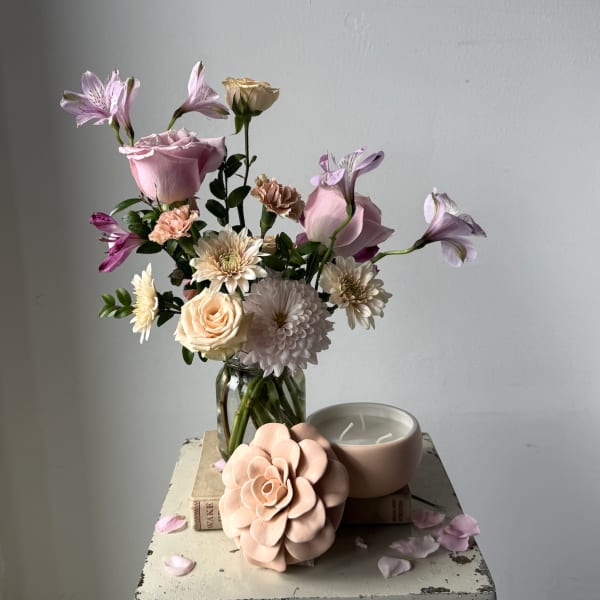 Mixed pastel bouquet in a glass vase beside a pink candle and flower-shaped decor