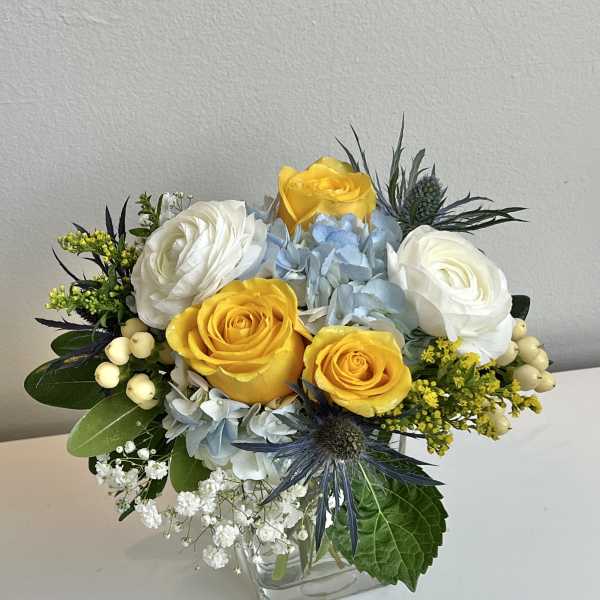 Bouquet of yellow and white roses with blue hydrangeas in a glass vase