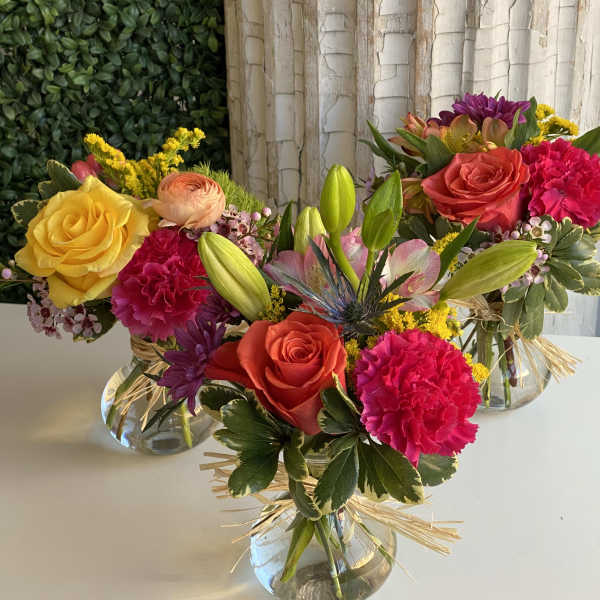 Three colorful mixed flower arrangements in clear glass vases