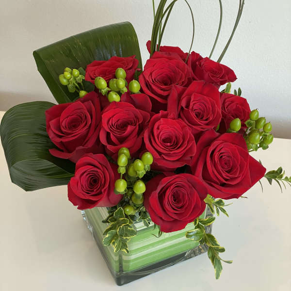 Red roses arranged in a square glass vase with green accents