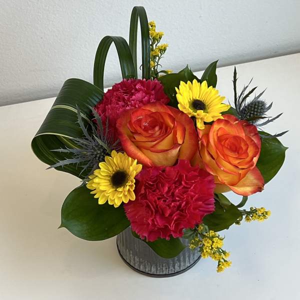 Bright bouquet of orange roses, pink carnations, and yellow daisies in a metal container