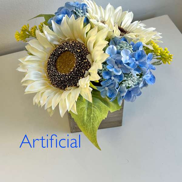 Artificial sunflower and blue hydrangea arrangement in a small wooden container