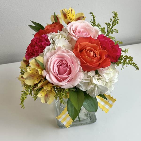 Mixed bouquet of roses, carnations, and white blooms in a glass vase