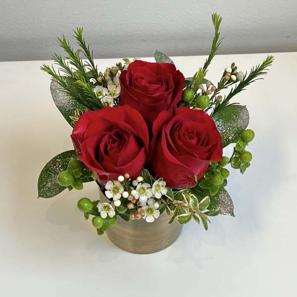 Three red roses in a small beige pot with white filler flowers
