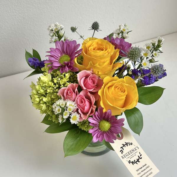 Bouquet of yellow and pink roses with purple daisies in a glass vase