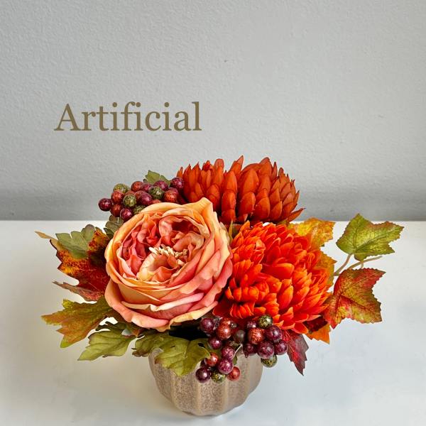 Artificial floral arrangement with orange blooms in a small vase